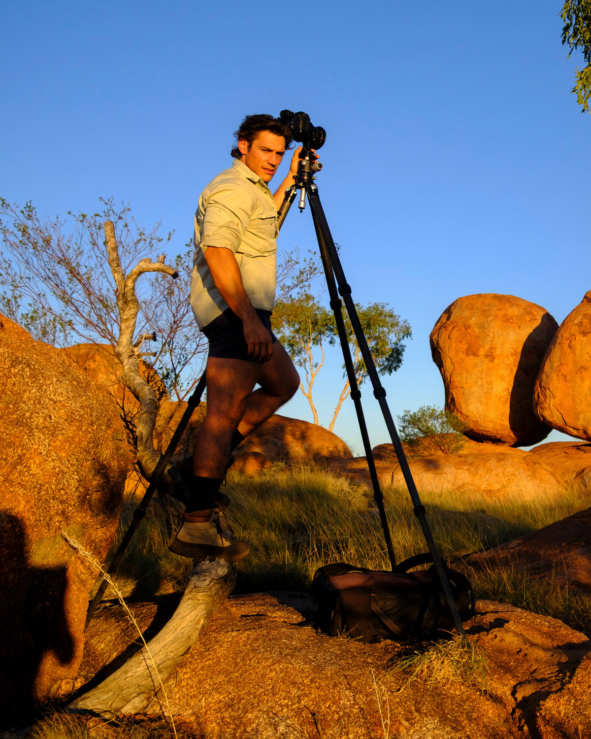 Mitchell Burns beside his tripod-mounted camera in a rocky Australian landscape.