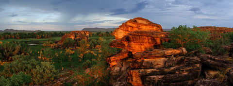 Kakadu Afterglow by Mitchell Burns — wet-season Kakadu National Park at sunset, glowing orange sandstone outcrop above green country and distant escarpments — illustrative Black + Black corner detail