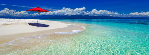 Red umbrella on the white sand of Undine Cay, surrounded by turquoise water off Port Douglas, Queensland — photograph by Mitchell Burns — illustrative Black + Black corner detail